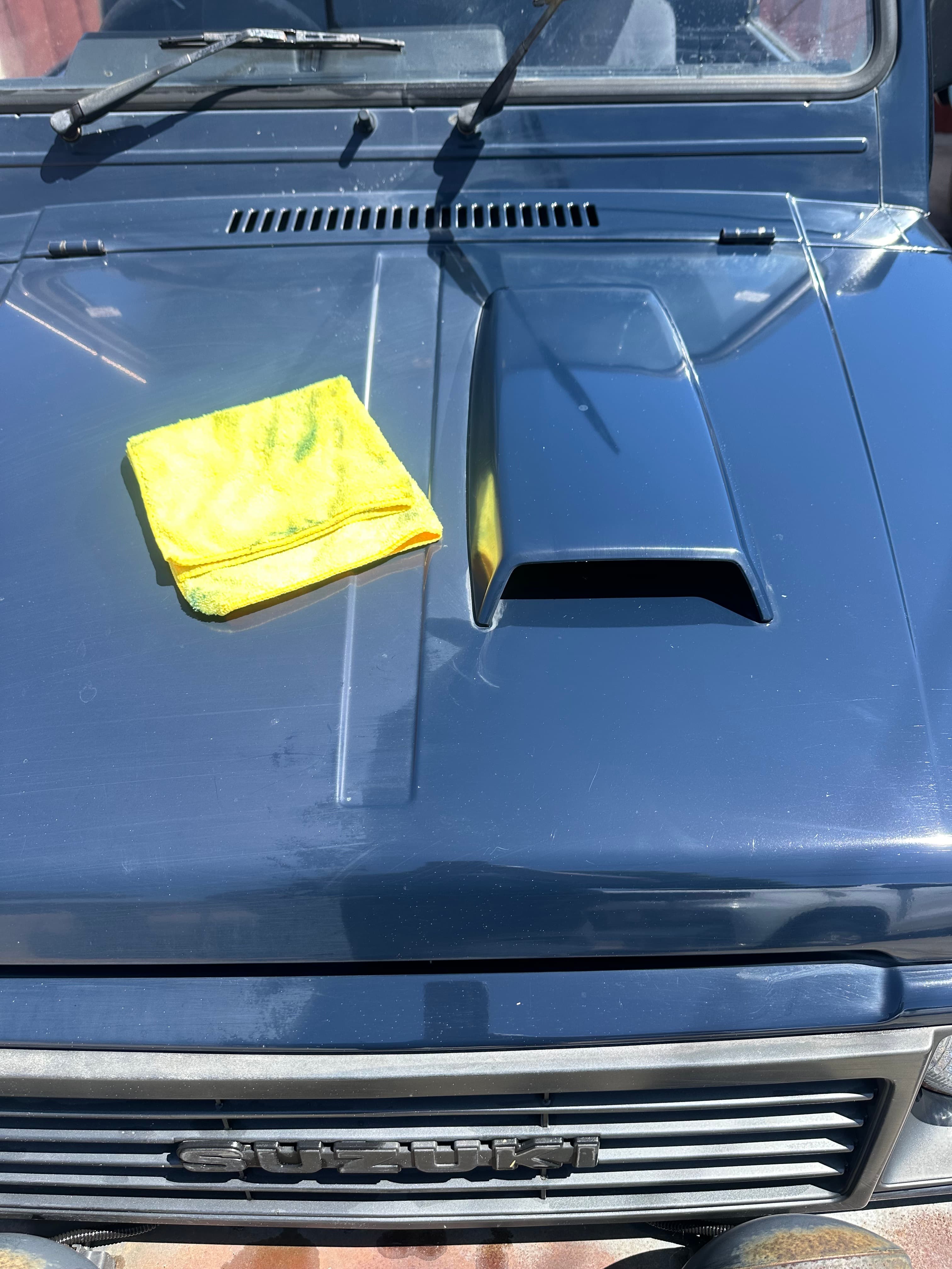 Yellow microfiber cloth on the blue hood of a Suzuki vehicle with hood scoop.